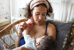 Infancy, motherhood, nutrition, lactation and breastfeeding concept. Indoor portrait of tender young mom nursing her baby boy, giving him all love and affection, sitting in bedroom