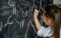 little girl schoolgirl near the chalkboard solves a chemistry problem. White coat and goggles. Offline education concept